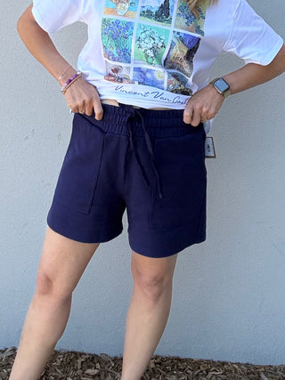 Person wearing a white t-shirt with colorful graphics and navy shorts against a plain background