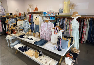 Clothing store interior with racks and tables displaying various clothing items and accessories.