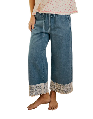 Woman wearing a pink and white top with lace sleeves and blue jeans on a white background