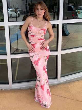 Woman in a pink floral dress standing in front of a store with large windows.