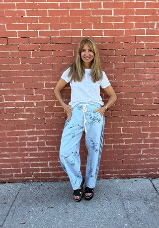 Woman wearing a white t-shirt and light blue pants standing against a red brick wall.
