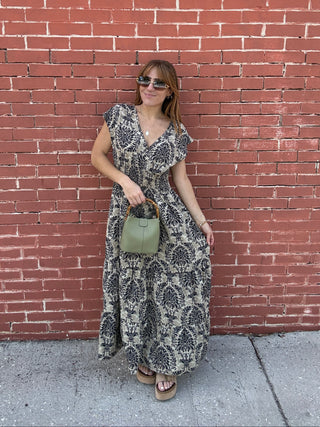 Woman lying on a red brick sidewalk with a patterned dress and sunglasses.