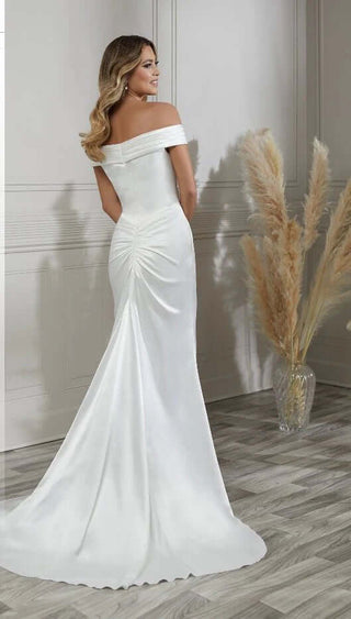 Woman in a white off-shoulder gown standing in a room with a neutral background