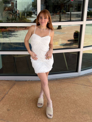 Woman in a white dress standing on a ledge with a building and window reflection in the background