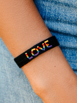 Pura Vida Woven Seed Bead Love Bracelet  Wear your love loud and proud with our Woven Seed Bead Love Bracelet. This bold black design features a thick woven band and “love” spelled out in a rainbow of seed beads.   For every bracelet sold, Pura Vida will donate 5% of the purchase price* to The Trevor Project, the world’s largest suicide prevention and crisis intervention organization for LGBTQ young people, with a minimum donation of $25,000. On arm. 